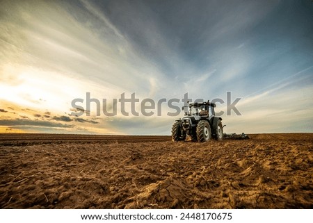 Wide-angle view of a tractor plowing farmland against a dramatic sunset sky