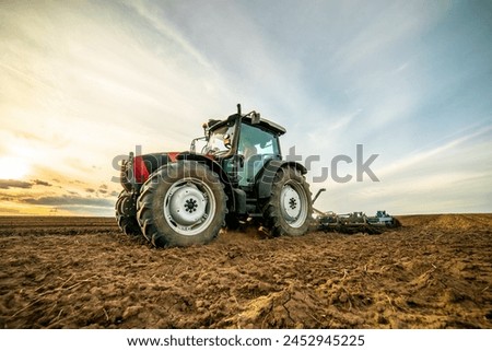 Wide-angle view of a tractor plowing farmland against a dramatic sunset sky