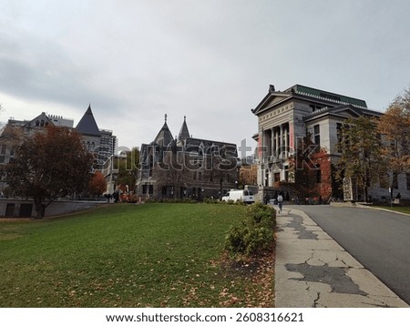A wide-angle view of a university campus with historic buildings, green lawns, and trees showing autumn colors under an overcast sky.