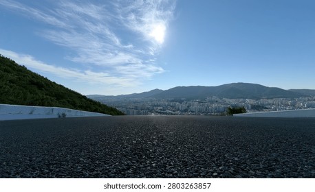 A wide-angle view of a vast mountain range under a bright, sunlit sky, with lush green hills in the foreground and a distant cityscape.