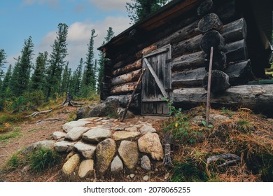A wide-angle view of a wooden forester's hut in a deep conifer taiga forest on the glade, built from a large log, with a stone porch on the ground covered by yellowed needles and rare grass - Shutterstock ID 2078065255