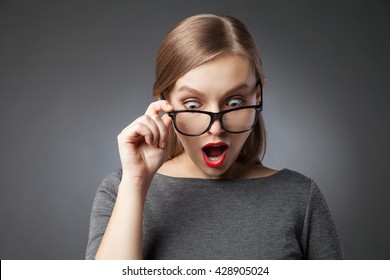 Wide-eyed woman in glasses looking down in amazement