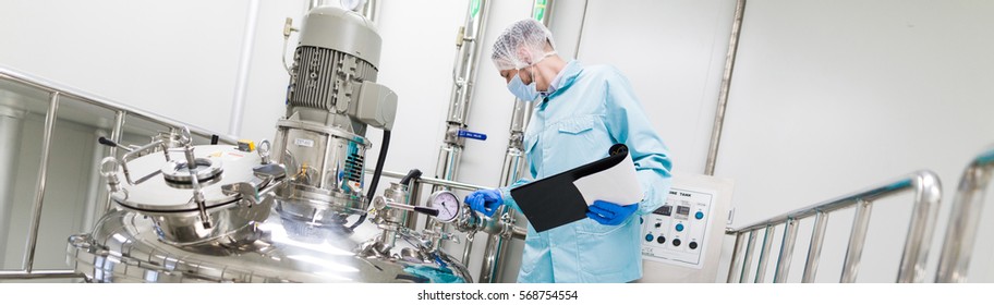 wide-screen picture, scientist in blue lab suit and gas mask working with control panel, look at steel tank, check readings - Shutterstock ID 568754554