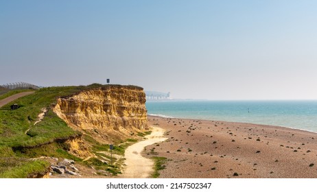 Widescreen view of the yellow sandstone cliffs and pebble beach at Glyne gap on the East Sussex coast in the United Kingdom with hazy blue sky on a spring day