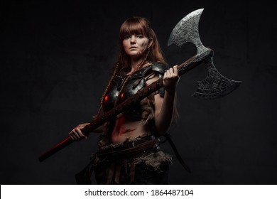 Wielding two handed axe grimy nordic amazon with brown hairs in dark armour posing in dark background.