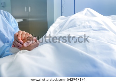 Wife holds the hand of the deceased spouse in the hospital.