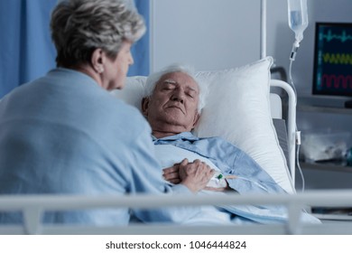 Wife Sitting On A Hospital Bed By An Elder Man In A Coma