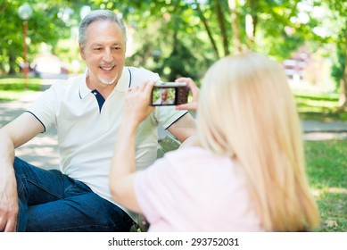 Wife using a compact camera to take a portrait of her husband in a park