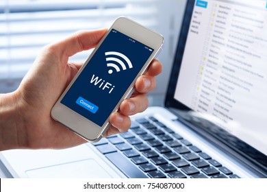 WiFi Symbol On Smartphone Screen With Button To Connect To Wireless Internet, Close-up Of Hand Holding Mobile Phone, Computer In Background