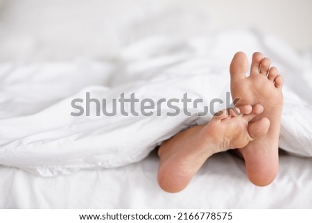 Wiggling toes of wakefulness. Shot of a pair of womans feet poking out from under the sheets of a bed.