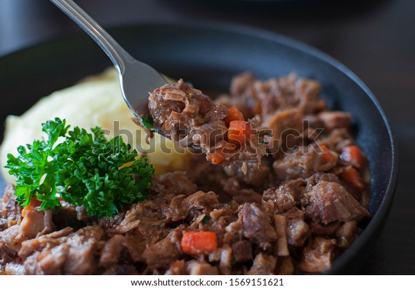 Wild boar stew or ragu or braised wild boar being
picked on fork with the dish blurred in background shot from high
angle under natural light