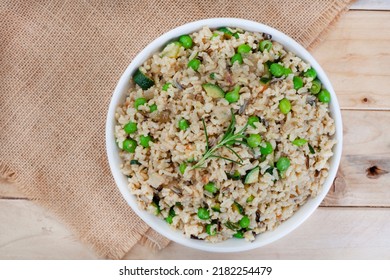 Wild And Brown Rice Pilaf With Green Peas, Onion And Baby Marrow On Rustic Wood With Burlap And Copy Space