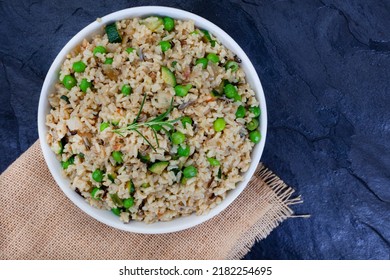 Wild And Brown Rice Pilaf With Green Peas, Onion And Baby Marrow On Black Slate With Burlap And Copy Space
