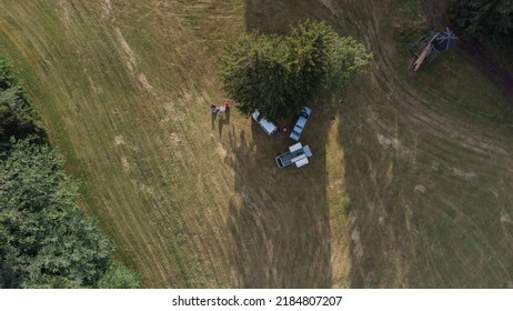 Wild Camping With Van Or Truck RV Gear. Aerial Drone Vertical View Of A Van Life Camp. Vanlife Style, Three Trucks Parked Next To A Tree With Campers Enjoying Next To A Table.