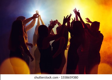 Wild. A Crowd Of People In Silhouette Raises Their Hands On Dancefloor On Neon Light Background. Night Life, Club, Music, Dance, Motion, Youth. Yellow-blue Colors And Moving Girls And Boys.