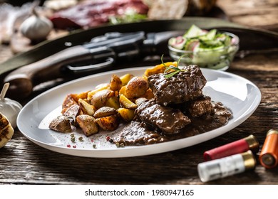 Wild Game Goulash Stew Served On A White Porcelain Plate With Roasted Potatoes And Seasoned With Four Colour Pepper Corn. Whole Food Is Surrounded By Hunting Shotgun And Gun Bullets.