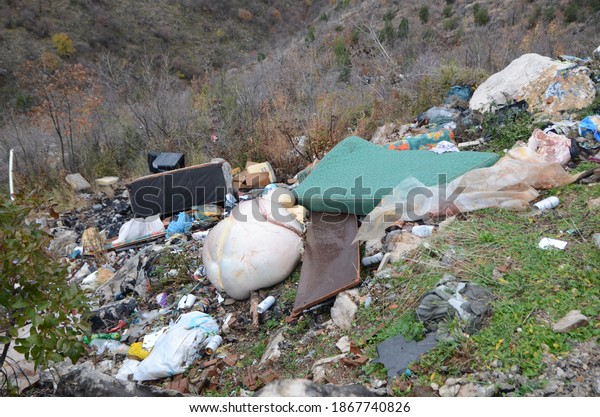 Wild garbage dump in nature. Open landfill\
site. Pile of garbage. Illegal dumping. Environmental pollution.\
Waste on landfill area. Animal offal,  plastic bottles, old\
furniture, car tires,\
packing...