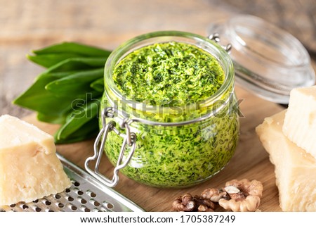 Wild leek pesto with olive oil and parmesan cheese in a glass jar on a wooden table. Useful properties of ramson. Leaves of fresh ramson