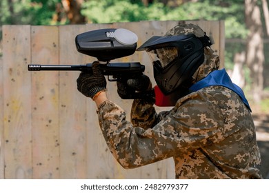 in the wild near tree structures player in a pintball uniform holds a pistol with a red balloon team game camouflage clothing