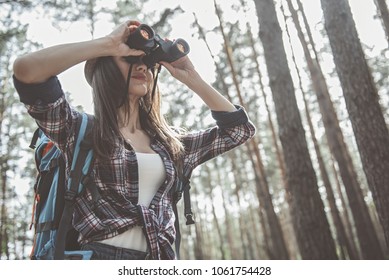 Wild place. Low angle of modern girl with backpack is looking through binoculars while standing in the forest. Copy space in the right side - Powered by Shutterstock