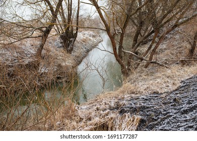wild stream in early spring in cloudy weather, weak water flow between high banks covered with trees, snowmelt and a peaceful landscape without people
