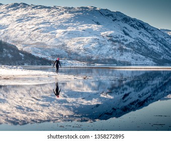 Wild Swim Woman In Wetsuit Walks Into Water With Snow On Mountains Reflected