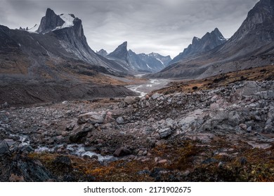 Wild Weasel river winds through  remote arctic valley of Akshayuk Pass, Baffin Island, Canada on a cloudy day. Dramatic arctic landscape with Mt. Breidablik and Mt. Thor. Autumn colors in the arctic.