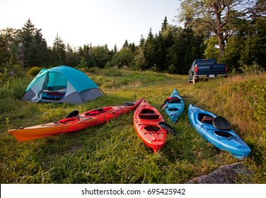 A Wilderness Campsite With A Pickup Truck, Four Colorful Kayaks, And A Pitched Tent In The Woods