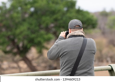 Wildlife Photographer Looking For Motifs Outdoor In The African Savannah With A System Camera With Full Frame Sensor, Photographed From Behind