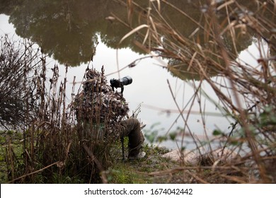 Wildlife Photographer Sitting And Camouflaged On The Bank Of A River Stalking Wild Animals.