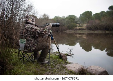 Wildlife Photographer Sitting And Camouflaged On The Bank Of A River Stalking Wild Animals.