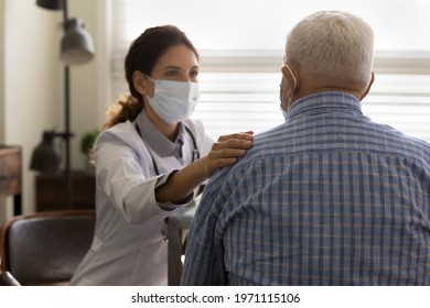 It Will Be All Right. Empathic Young Female Doctor In Medical Mask On Face Hold Hand On Shoulder Of Elderly Man Patient Encourage To Fight With Disease. Supportive Woman Gp Comforting Old Male Client