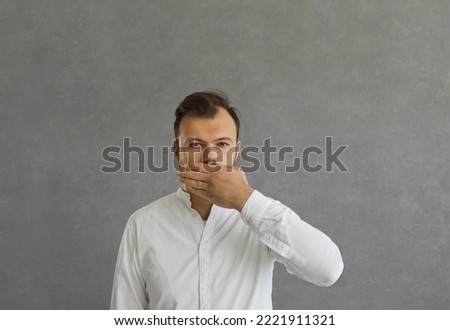 I will be quiet. Portrait of a handsome serious man closes his mouth with his hand while standing on a gray concrete background. Man shows that he has a secret without disclosing information.