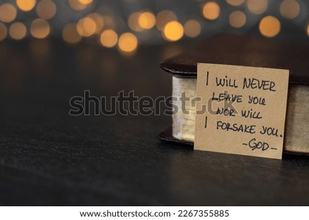 I will never leave you nor will I forsake you-God, handwritten verse on note and holy bible with golden pages with blurred golden bokeh background.