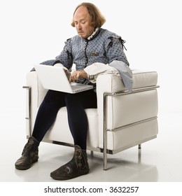 William Shakespeare In Period Clothing Sitting On Modern Chair Using Laptop.