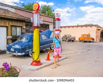 Williams, Arizona, United States - June 14, 2006: Smiling And Posing Young Tourist Near To A Classic Cadillac Car And A Old Vintage Gas Pump Service Station On The Famous Road 66 In Town