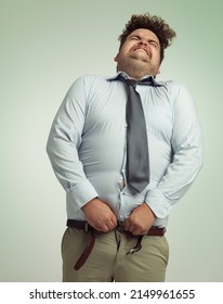 Willing his pants closed. Humorous studio shot of an overweight businessman trying to button his pants.