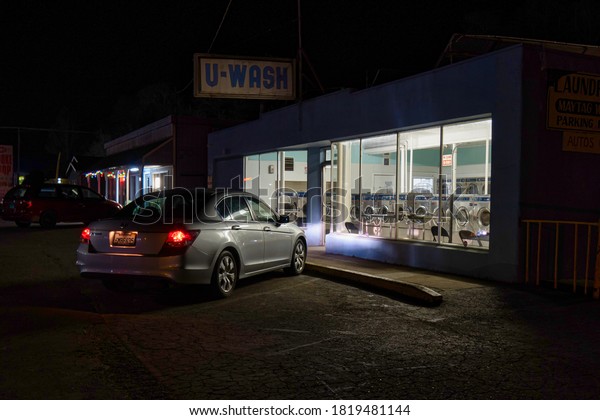 Willits,\
United States - February 2020: a car is parked and illuminated\
infront of a laundry dry cleaning store at\
night
