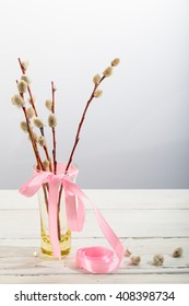 Willow branches with a pink tape in a transparent vase. A bouquet for a Palm Sunday, a light background, a wooden white table, soft focus