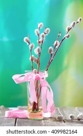 Willow branches with a pink tape in a transparent vase. A bouquet for a Palm Sunday, a flavovirent background, a wooden white table, soft focus