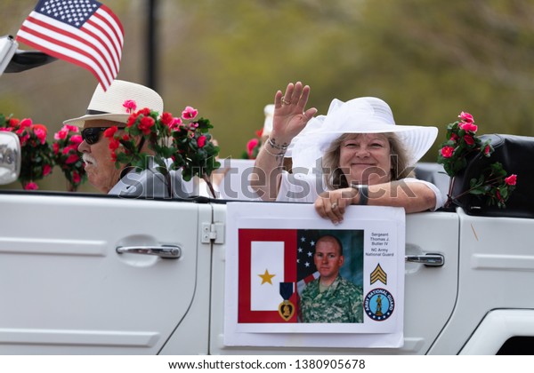 Wilmington, North Carolina, USA - April 6, 2019:\
The North Carolina\
Azalea Festival, Man driving a classic\
Volkswagen with a woman holding the photograph of a member of the\
NC Army National\
Guard