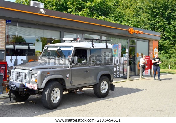 Wilsele, Vlaams-Brabant, Belgium - August, 24,\
2022: adult blond woman and red hair young man leaving shop in\
front of stationary Landrover Defender parked in front of Carrefour\
Express shop and Lukoi