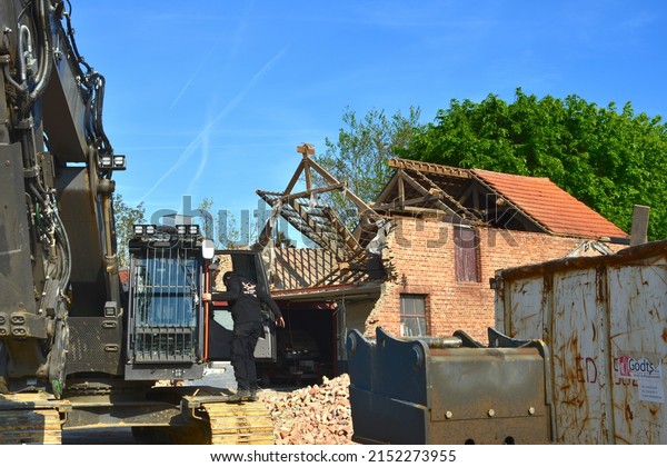 Wilsele, Vlaams-Brabant,\
Belgium - May 03, 2022:  Volvo excavator dismantling a car repair\
garage building in brick. Construction driver entering bulldozer\
cabin