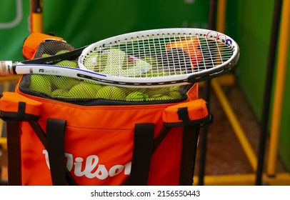 A lot of Wilson brand tennis balls and a tennis rocket placed on top of it on a clay ground preparing for a training. Sports industry. Romania, 2022.