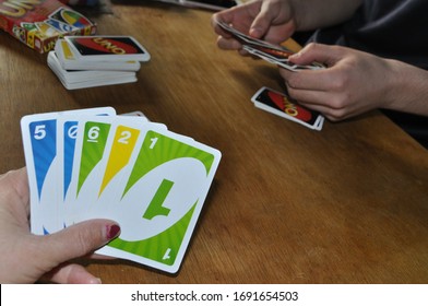 Wiltshire / UK - April2, 2020:  Family Members Playing UNO Game On Wooden Table During Covid-19 Pandemic.