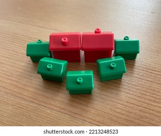 Wiltshire, UK - October 2022: Monopoly Red Hotel And Green House Building Pieces On A Wooden Table