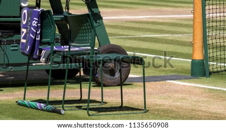 Wimbledon London, July 2018. Players' chairs with towel folded over the back, and a green and purple umbrella on the grass. Towel has the name Djokovic on it. 