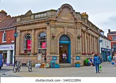 Wimborne Minster, Dorset / England - 6/25/2019: White Stuff Retail Clothing Shop In The Central Square Of Wimborne In The Former HSBC Bank Building.Young Woman With Bag Outside.Lady Leaving Store.