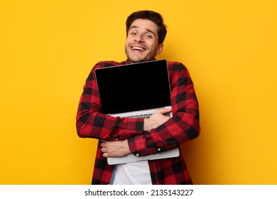 Win Concept. Portrait of overjoyed excited young man hugging notebook with black empty screen, holding it tight near chest. Positive male nerd posing isolated over yellow studio background wall - Shutterstock ID 2135143227