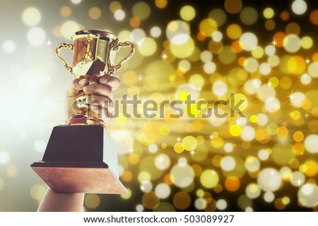 Win concept,Man holding up a gold trophy cup is winner in a competition with gold background.